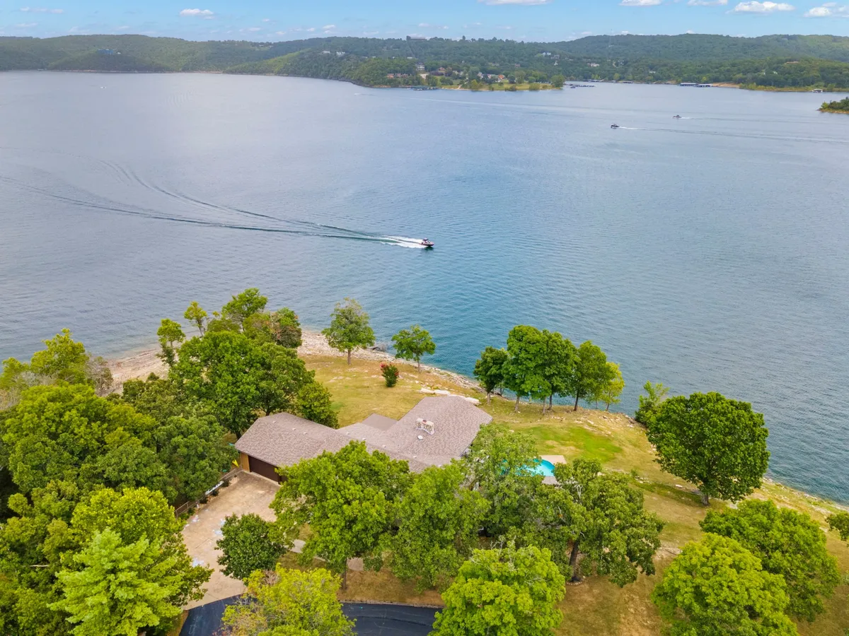 A picturesque exterior scene featuring the lake, the house, a swimming pool, and a docked boat. The image emphasizes the property's lakeside setting and easy water access, while the visible boat reinforces the boating lifestyle.
