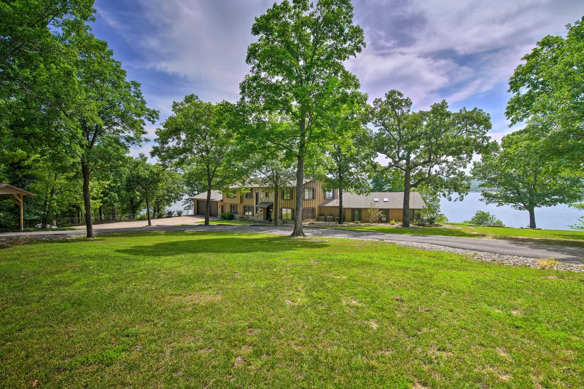 A wide, serene view of the property’s spacious lawn, large trees, and the lake beyond, with modern architecture in the background. The space invites guests to gather for picnics, stargazing, or simply enjoying the natural setting.