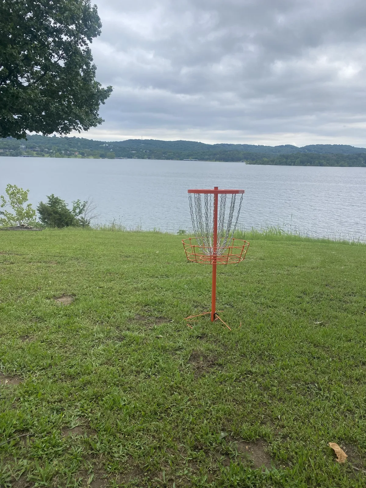A disc golf basket stands ready on a green lawn with the lake and trees in the background. The setting sun casts a relaxed glow, hinting at shared fun and friendly competition in the great outdoors.