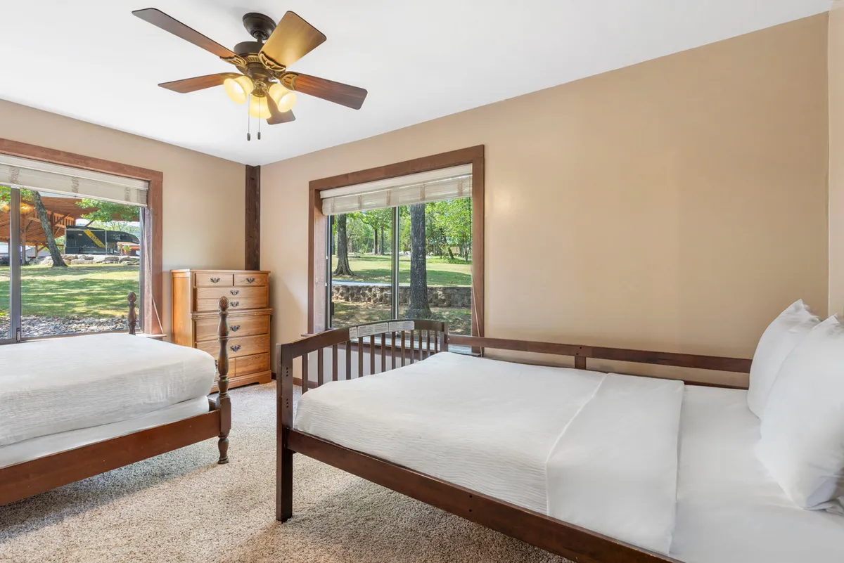 A comfortable bedroom with two beds, large windows that provide nature views, a dresser, and a ceiling fan. The space is bright and inviting—ideal for flexible sleeping arrangements such as families or groups of friends.