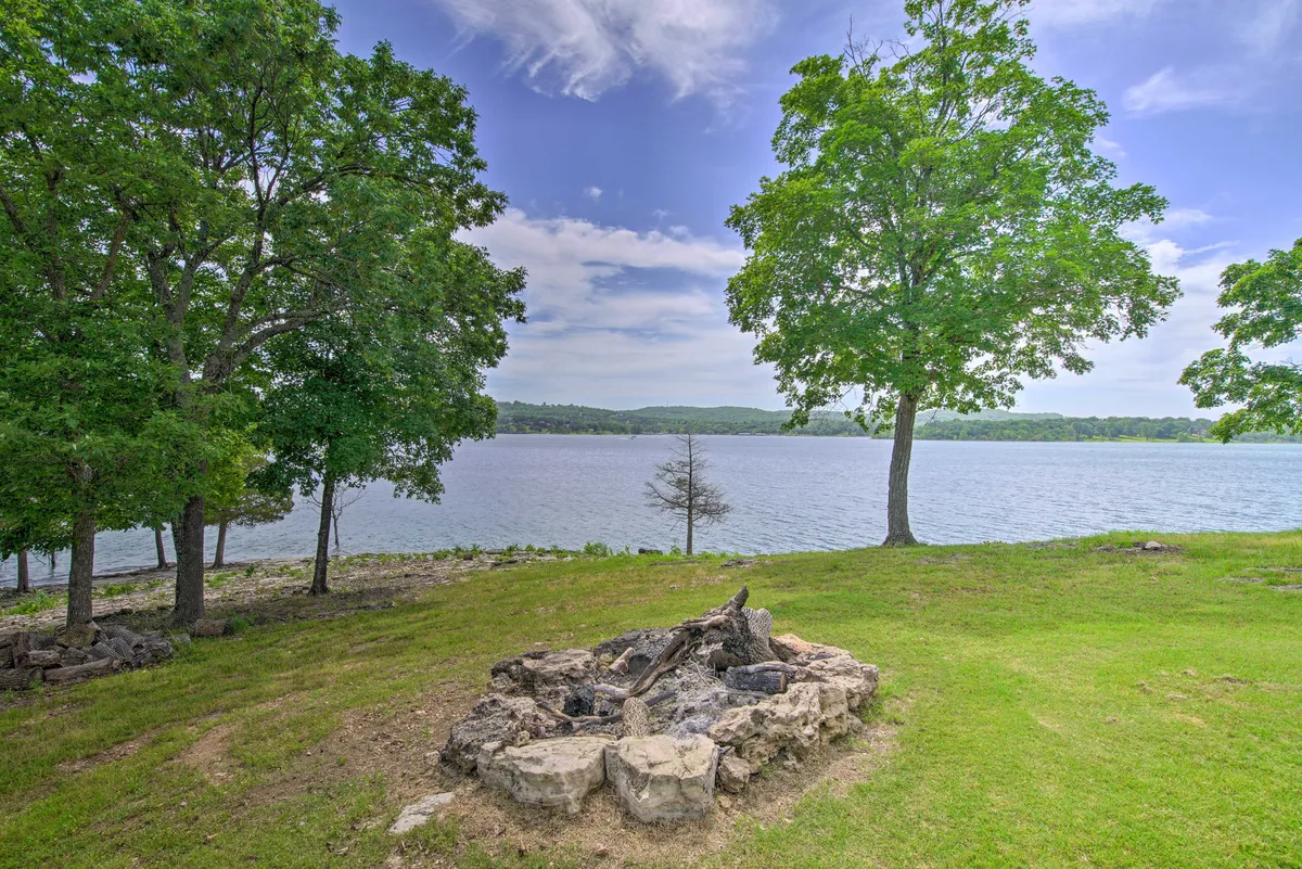A rustic campfire pit sits by the lakeshore, surrounded by trees, with the tranquil lake and sky stretching out behind. This cozy setup evokes evenings of storytelling, s’mores, and togetherness around the fire.