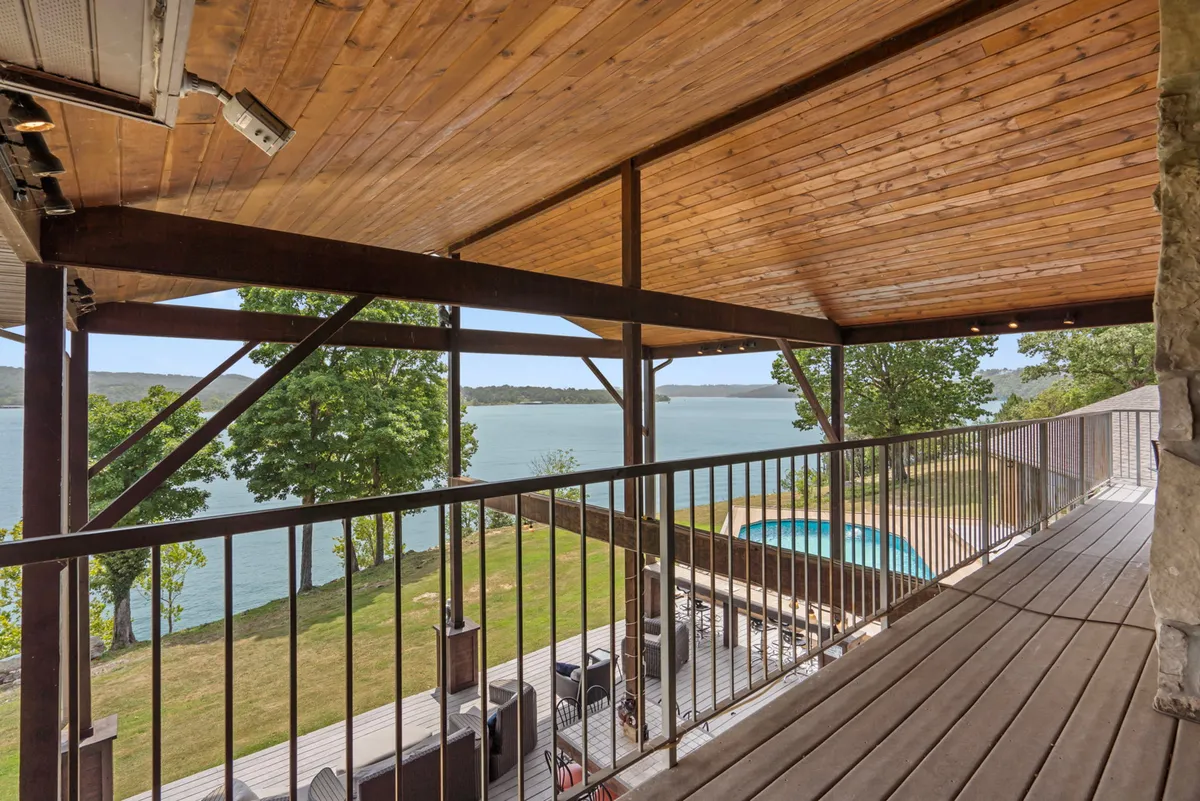 An inviting exterior scene featuring a sparkling swimming pool beside a tranquil lake. Comfortable outdoor seating provides a perfect area for lounging or socializing, with beautiful landscaping and water views completing the summer retreat atmosphere.