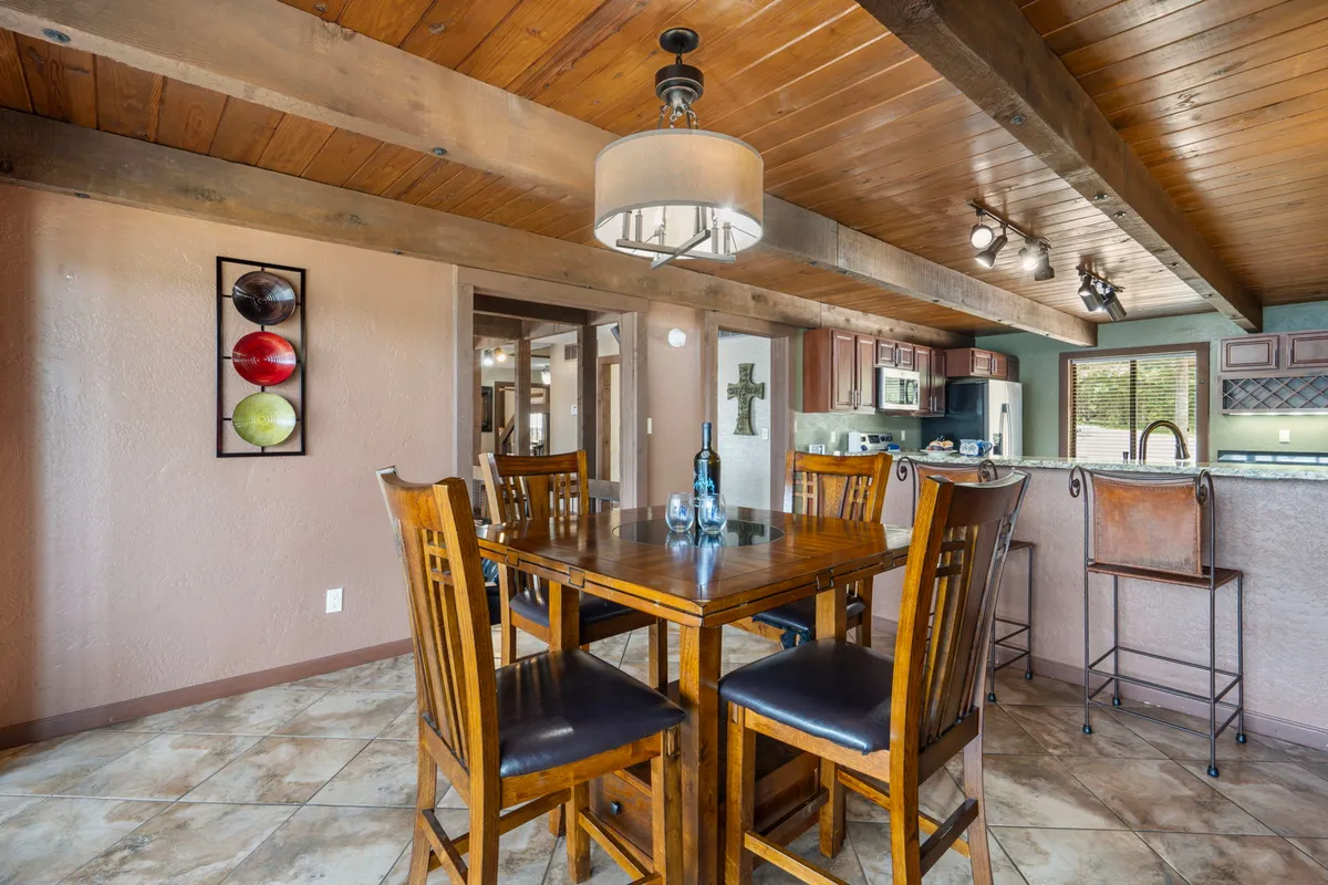 This image captures the dining area, featuring a wooden table, bar stools along a kitchen peninsula, and warm artwork on the wall. The setup is ideal for family meals, social gatherings, and seamlessly connects to the kitchen, underscoring the open-concept design.