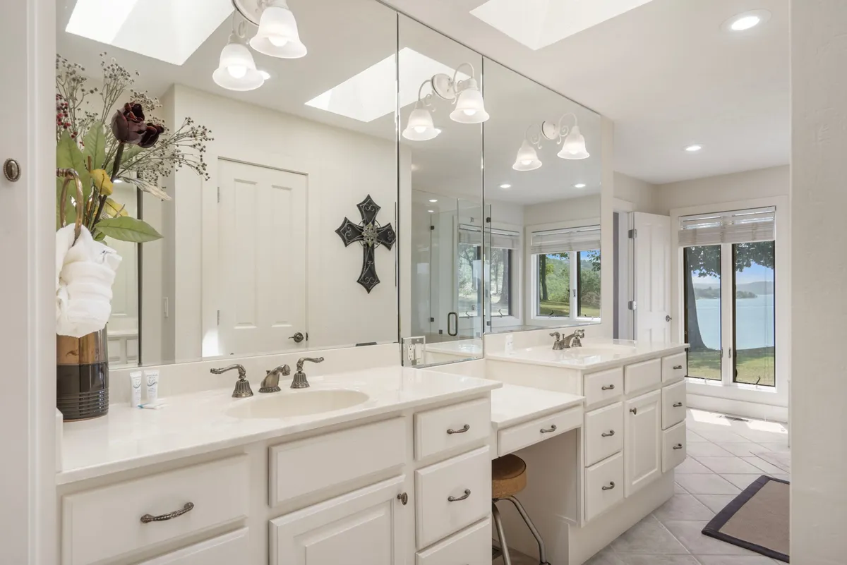 A bright, modern bathroom with double vanity sinks, large mirrors, and skylights offering a partial view of the lake. The refreshing atmosphere is perfect for morning routines or unwinding after a long day.