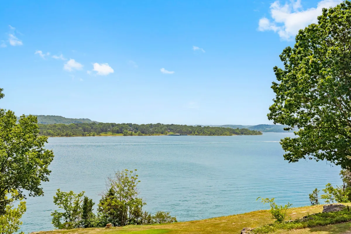 A tranquil view of Table Rock Lake bordered by lush greenery and distant hills. The calm waters are ideal for boating, fishing, and other water activities, offering a picturesque natural setting that beckons outdoor adventure.