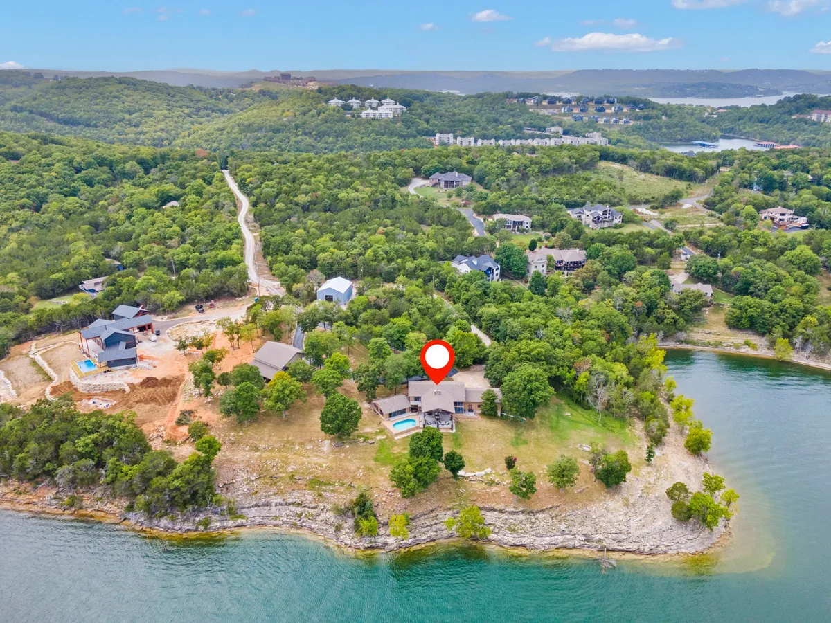 An exterior shot showing the main house with a swimming pool, seating area, and a clear view of the lake surrounded by greenery. The space is inviting for both water activity and group gatherings, emphasizing the proximity to the lake and ample space for family fun.