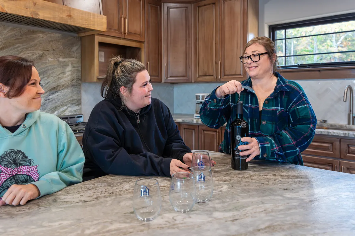 This lively kitchen scene centers on a spacious kitchen island where three women are socializing and preparing food. The kitchen is modern and fully equipped, with sleek appliances and plenty of workspace, highlighting both functionality and a space for creating memories together.